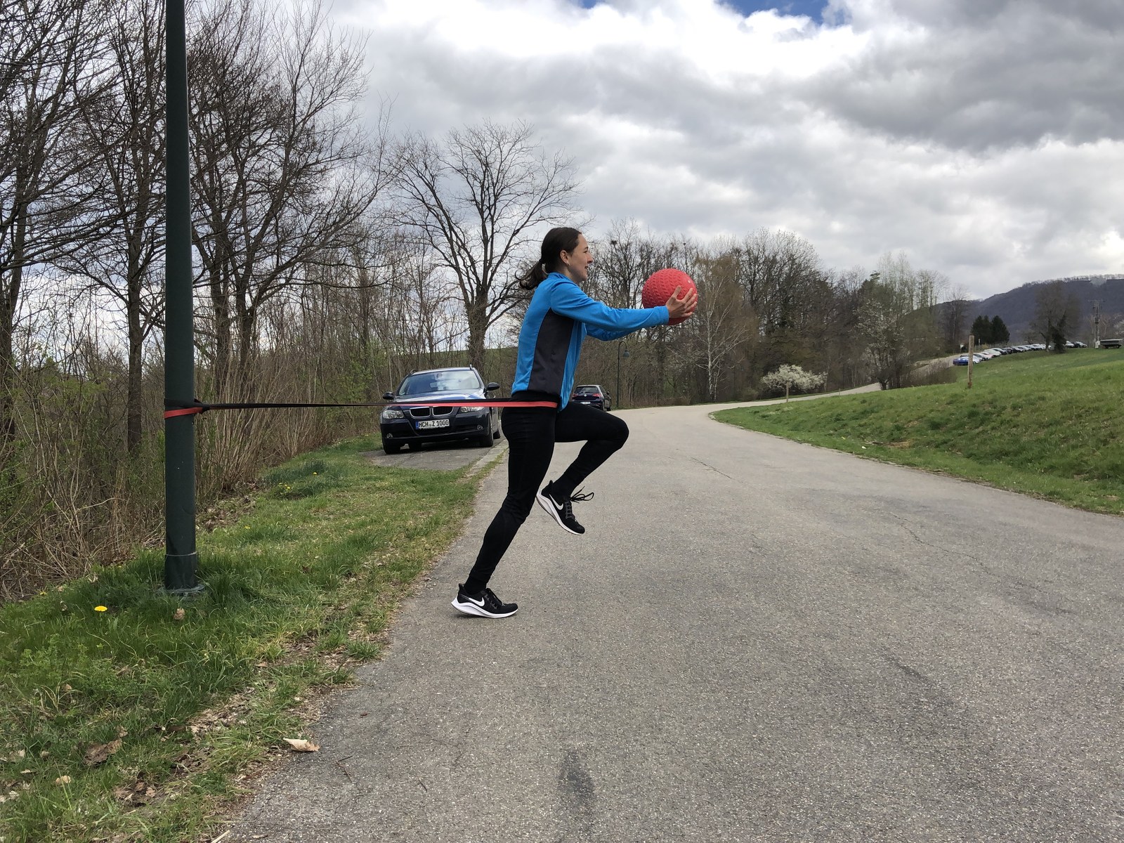 Einbeinige Athletikübung mit Widerstandsband und rotem Ball im Freien.